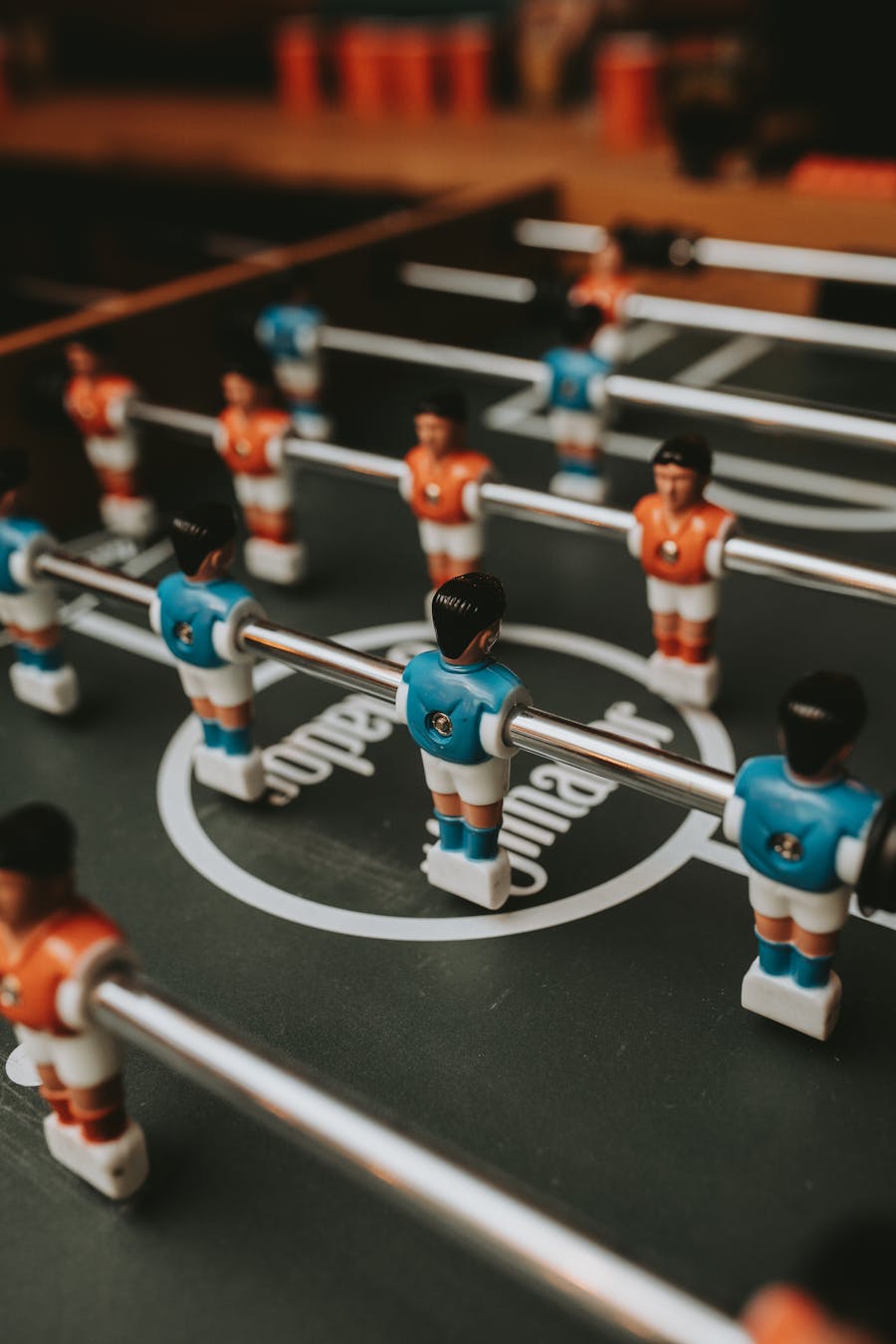 Close-up of a foosball table showing blue and orange player figures mounted on rods.