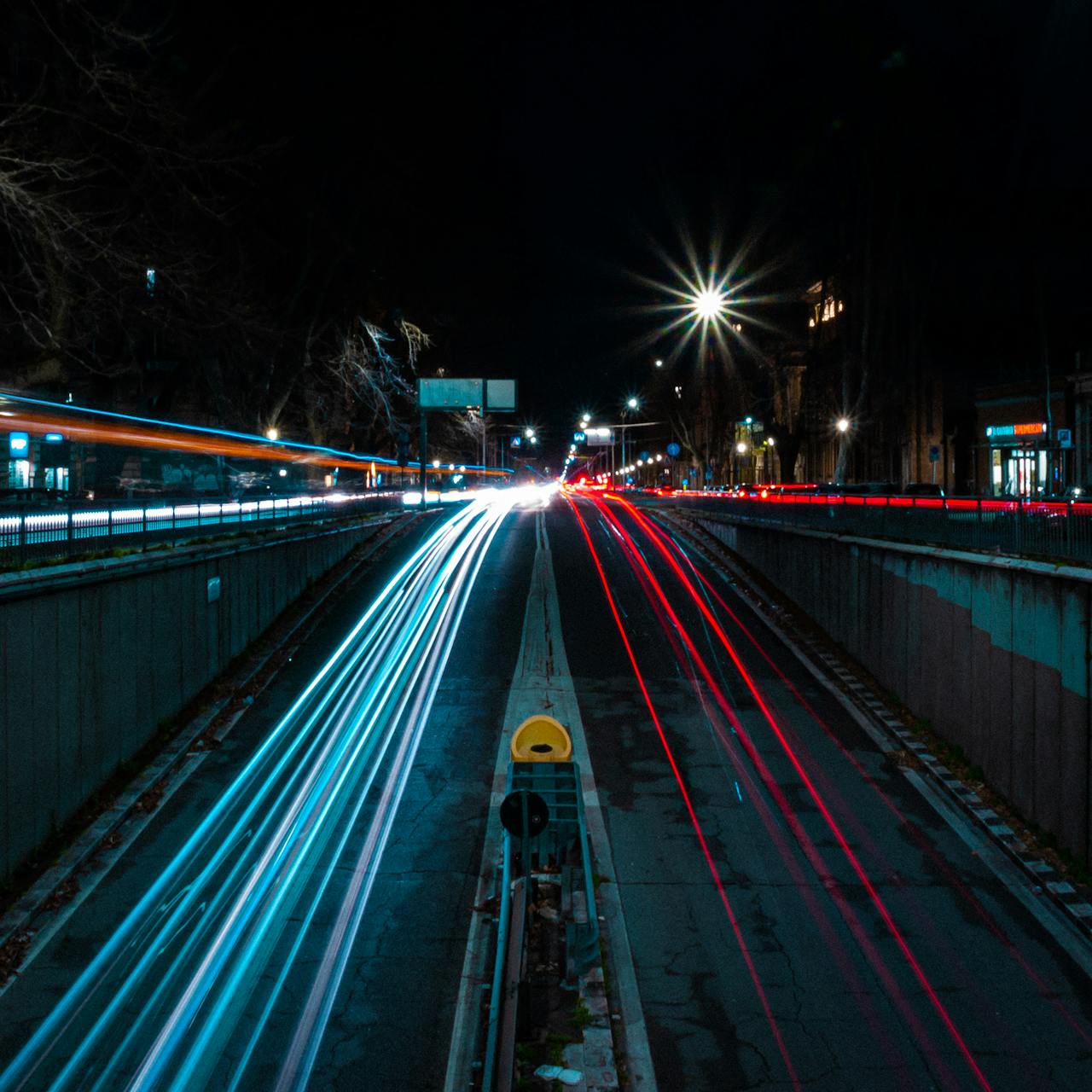 Long exposure of a night highway showing blue and red light trails from passing vehicles.