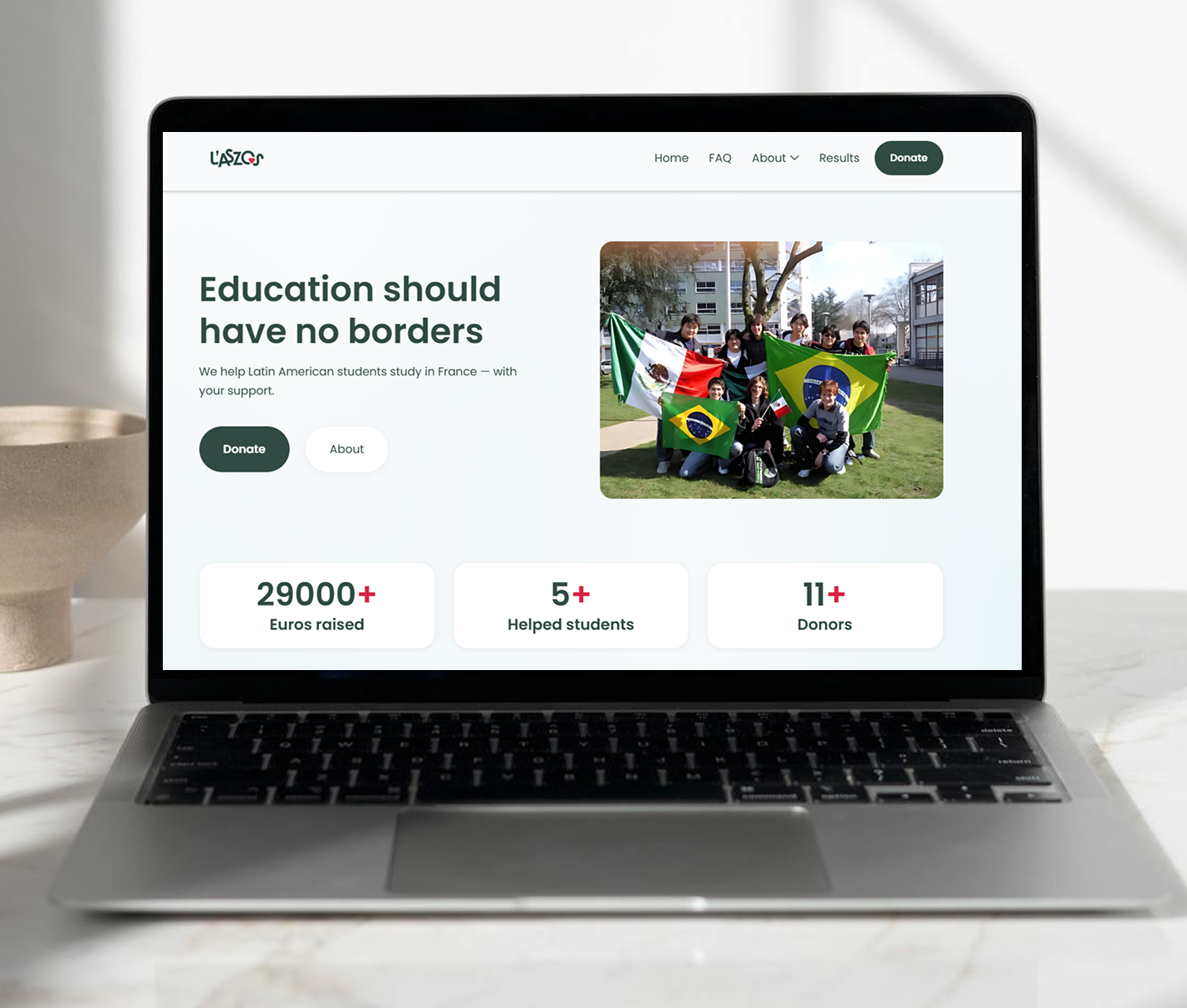 Laptop showing a website homepage with the headline 'Education should have no borders', a group photo of students holding Mexican and Brazilian flags, and fundraising stats including 29000+ euros raised, 5+ helped students, and 11+ donors.