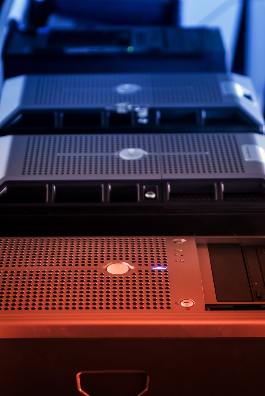 Close-up view of stacked server hardware with perforated panels and indicator lights in blue and red lighting.
